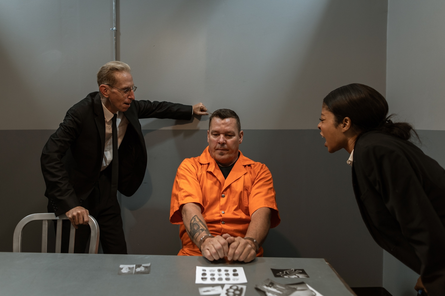 Man in orange jumpsuit in handcuffs being interrogated.